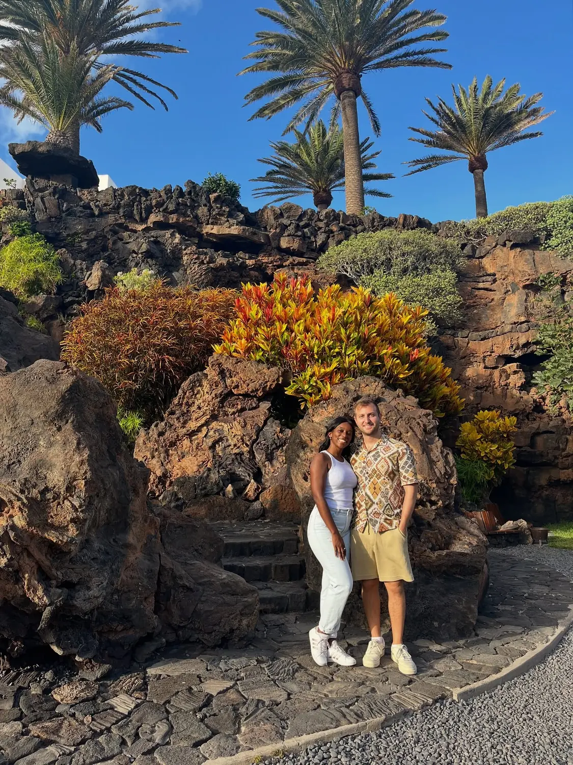 Us in a lush lava garden with tall palms rising over dark volcanic rock and colourful plants