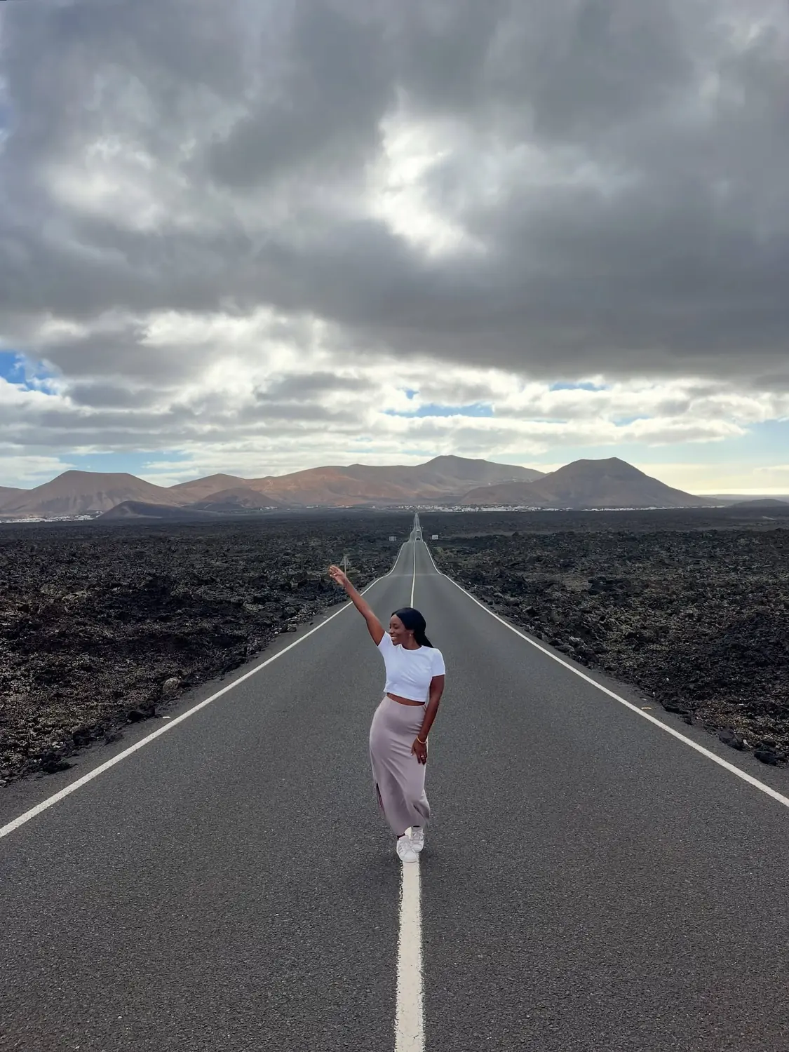 Melody standing on the centre line of a dead-straight road cutting through black lava fields toward distant mountains