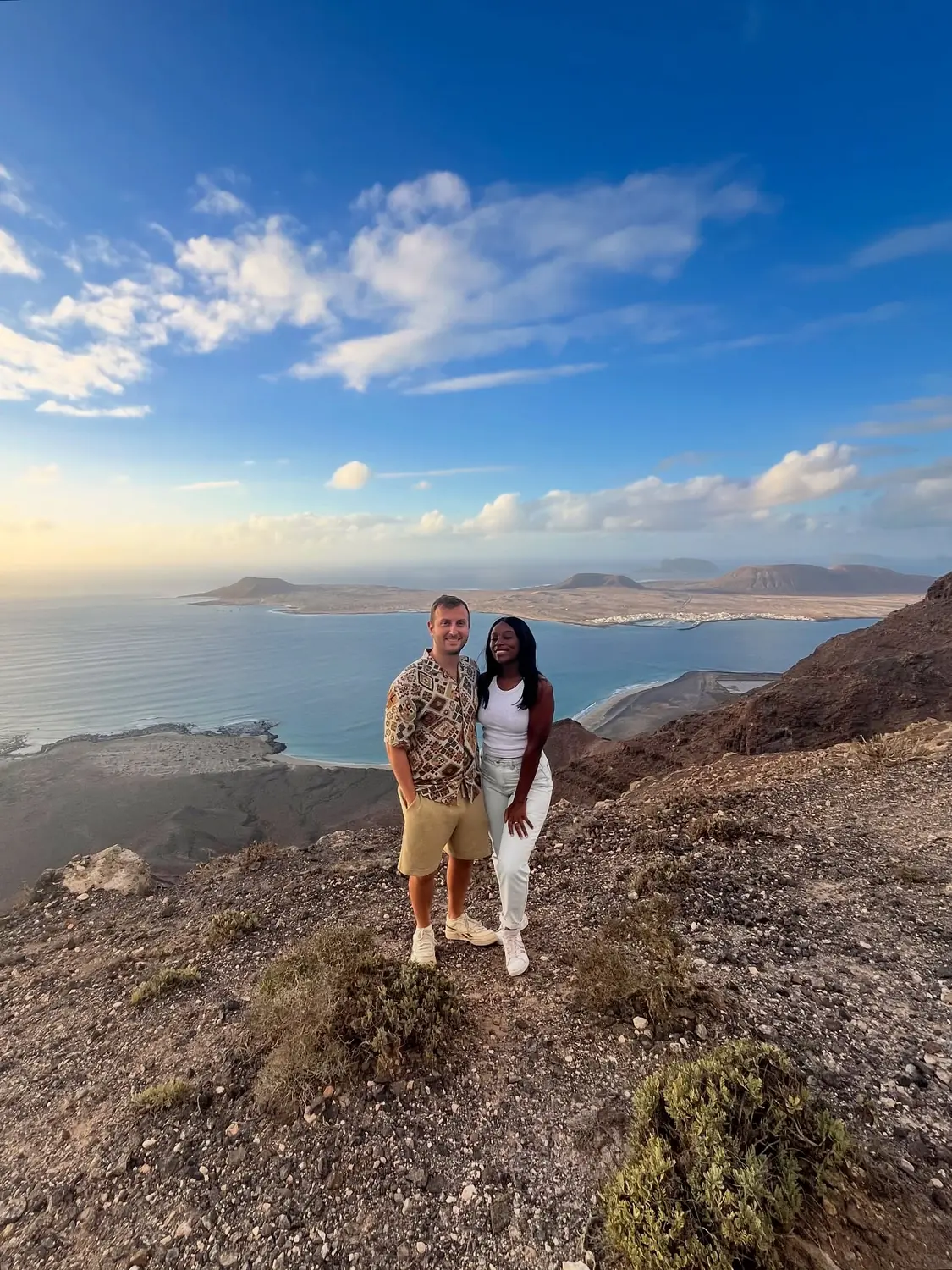 Us at a clifftop viewpoint at golden hour looking over the island of La Graciosa and the sea, Lanzarote