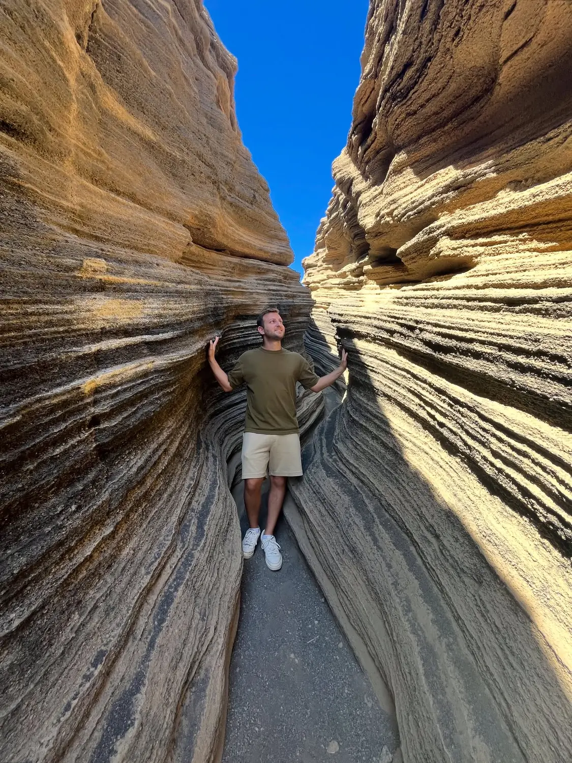 Andrew standing between the smooth striped sandstone walls of a narrow slot canyon