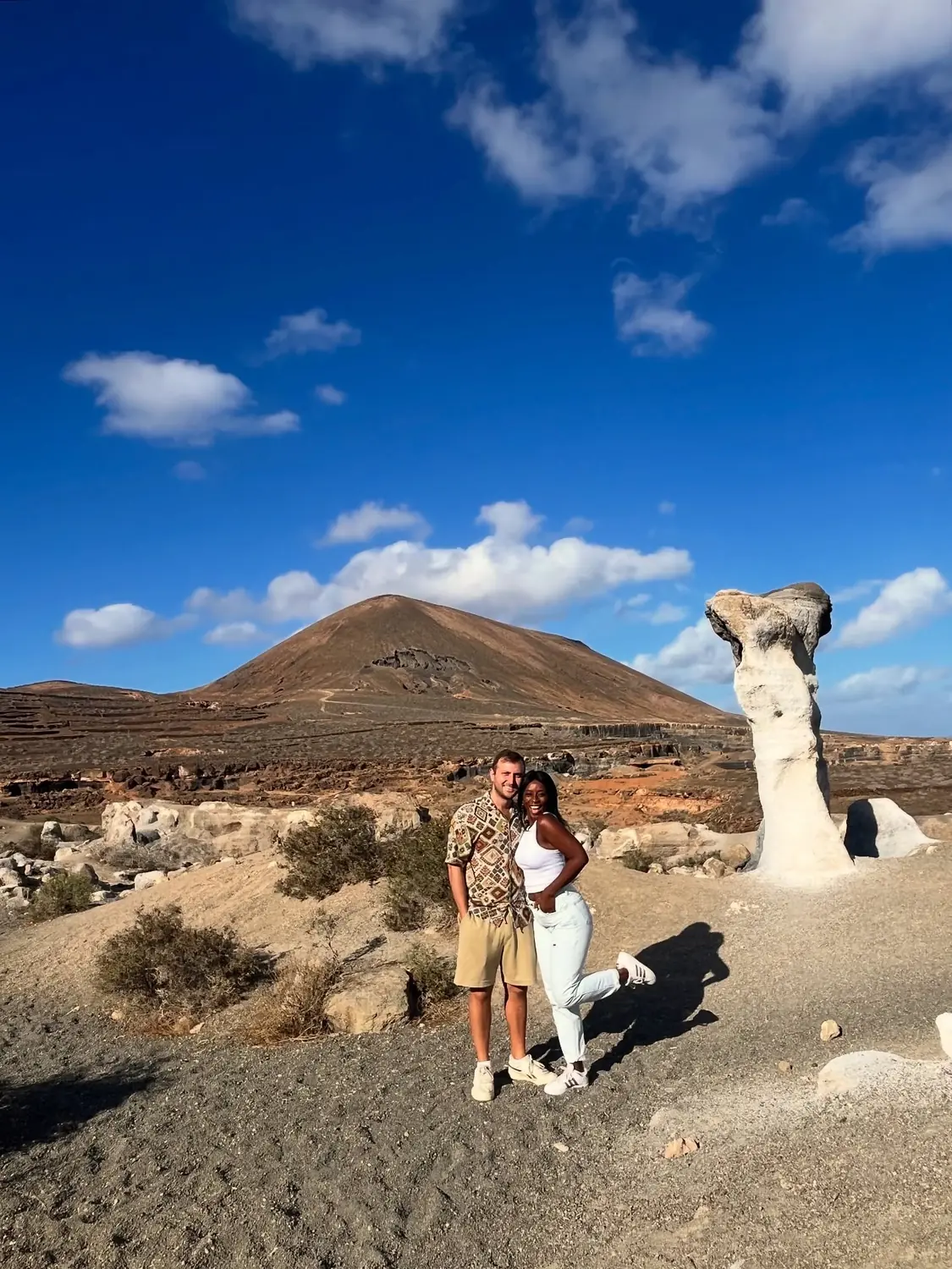 Us posing by a tall white rock formation with a brown volcano behind under blue sky