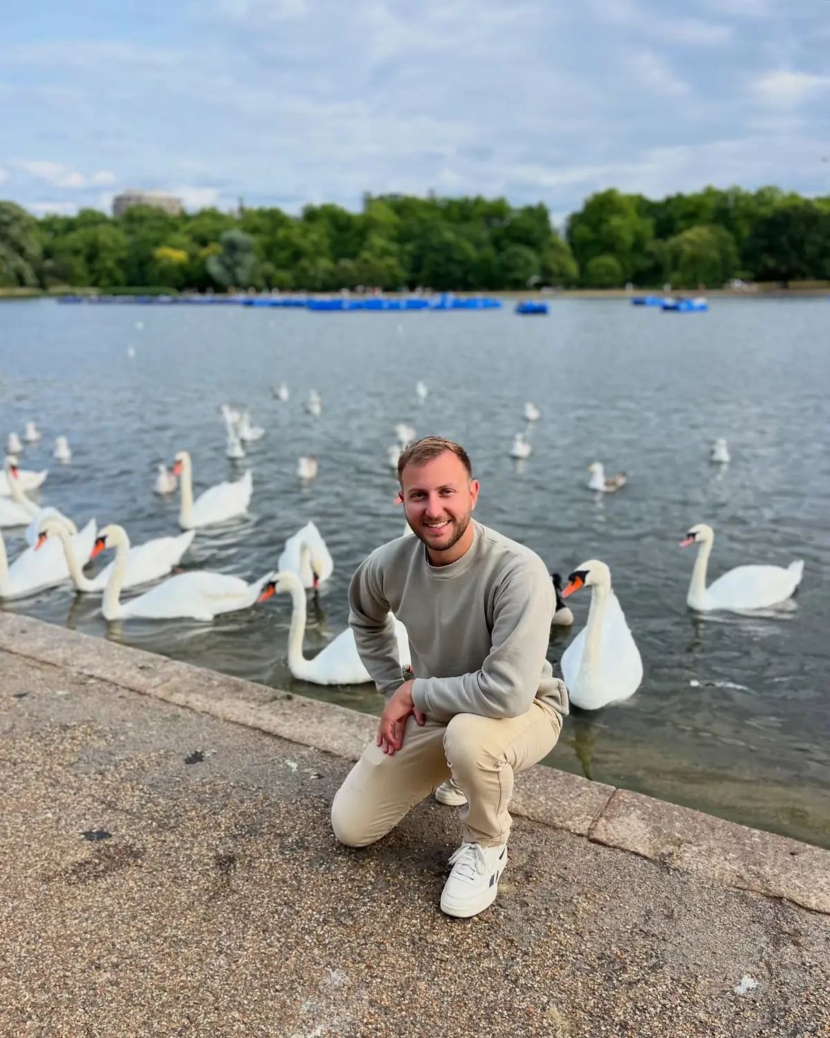 Andrew crouched by the water surrounded by white swans in Hyde Park