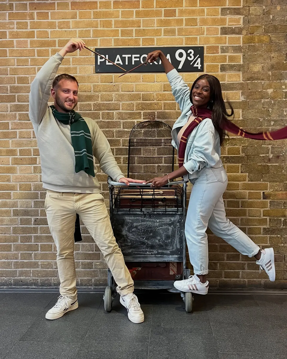 Us posing with wands at the Platform 9¾ trolley disappearing into the wall at King's Cross
