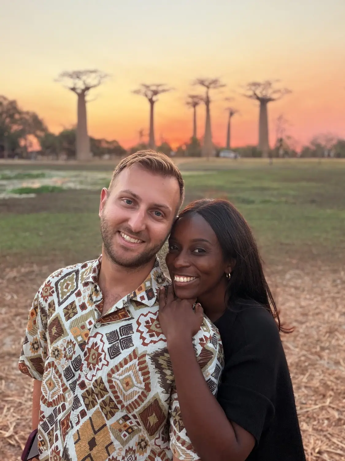 Us smiling together with a row of baobabs glowing against an orange sunset
