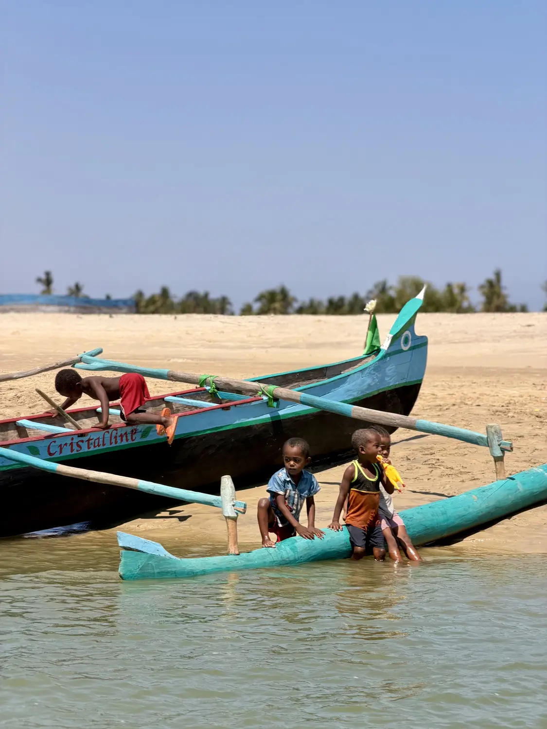 Children playing on a brightly painted outrigger pirogue at the water's edge