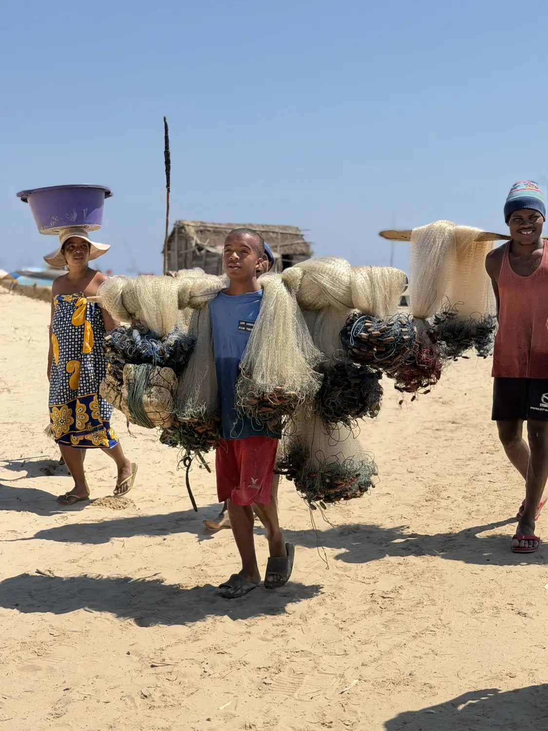 A young fisherman carrying bundles of fishing nets across the sand in Betania