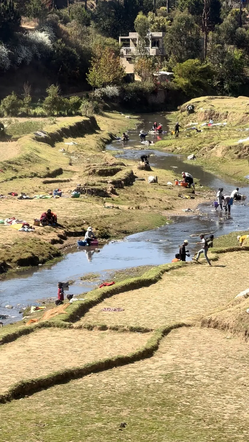 Villagers washing clothes in a shallow river and laying them out to dry on the grassy banks