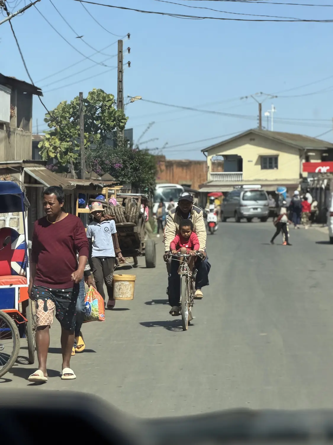 Everyday street life in a Malagasy town: a man cycling with a child, people carrying shopping