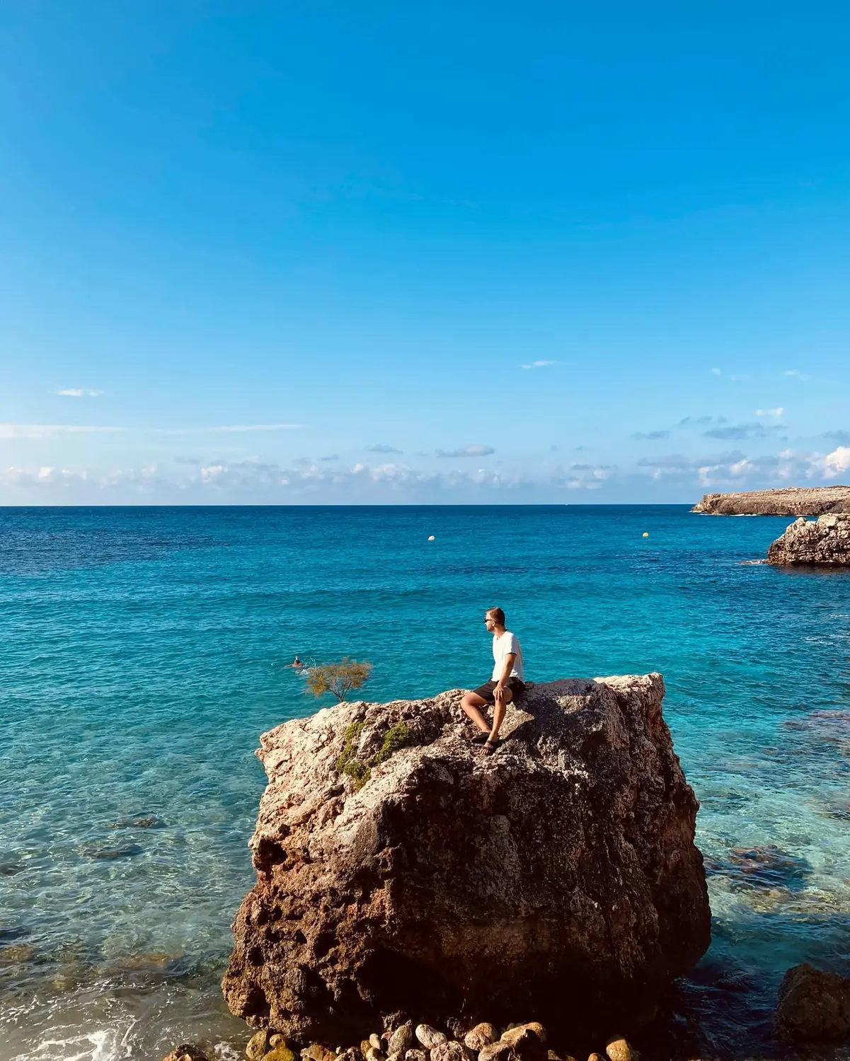 Andrew sitting on a large rock surrounded by crystal-clear water in Mallorca