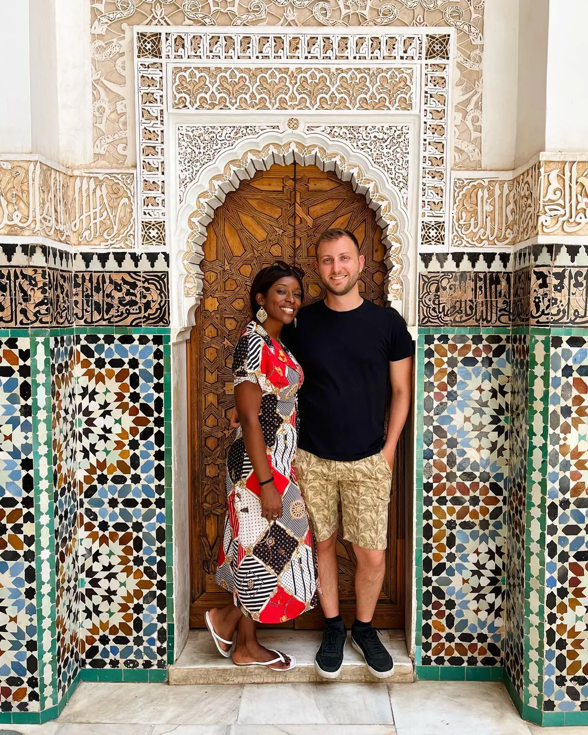 Us framed by a carved cedar door and intricate zellij tilework in a Marrakesh palace