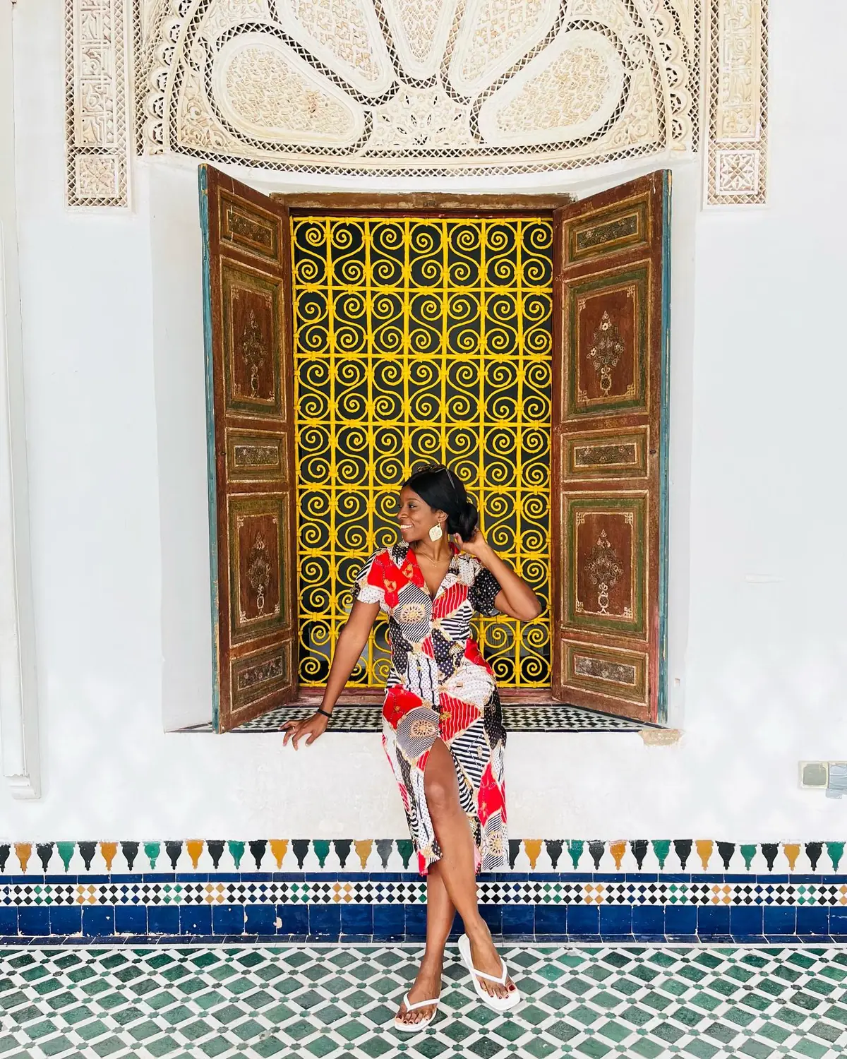 Melody by an ornate yellow wrought-iron palace window above bands of zellij tile