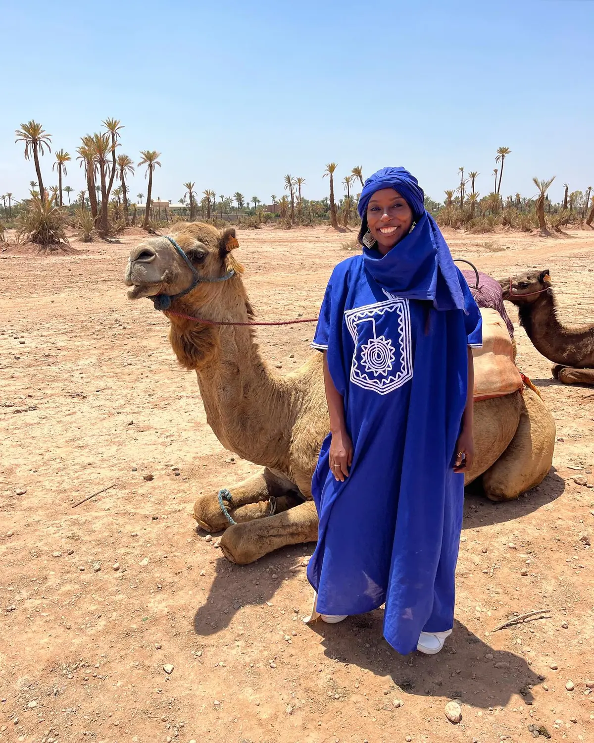 Melody in a blue Berber robe beside a resting camel in the Palmeraie