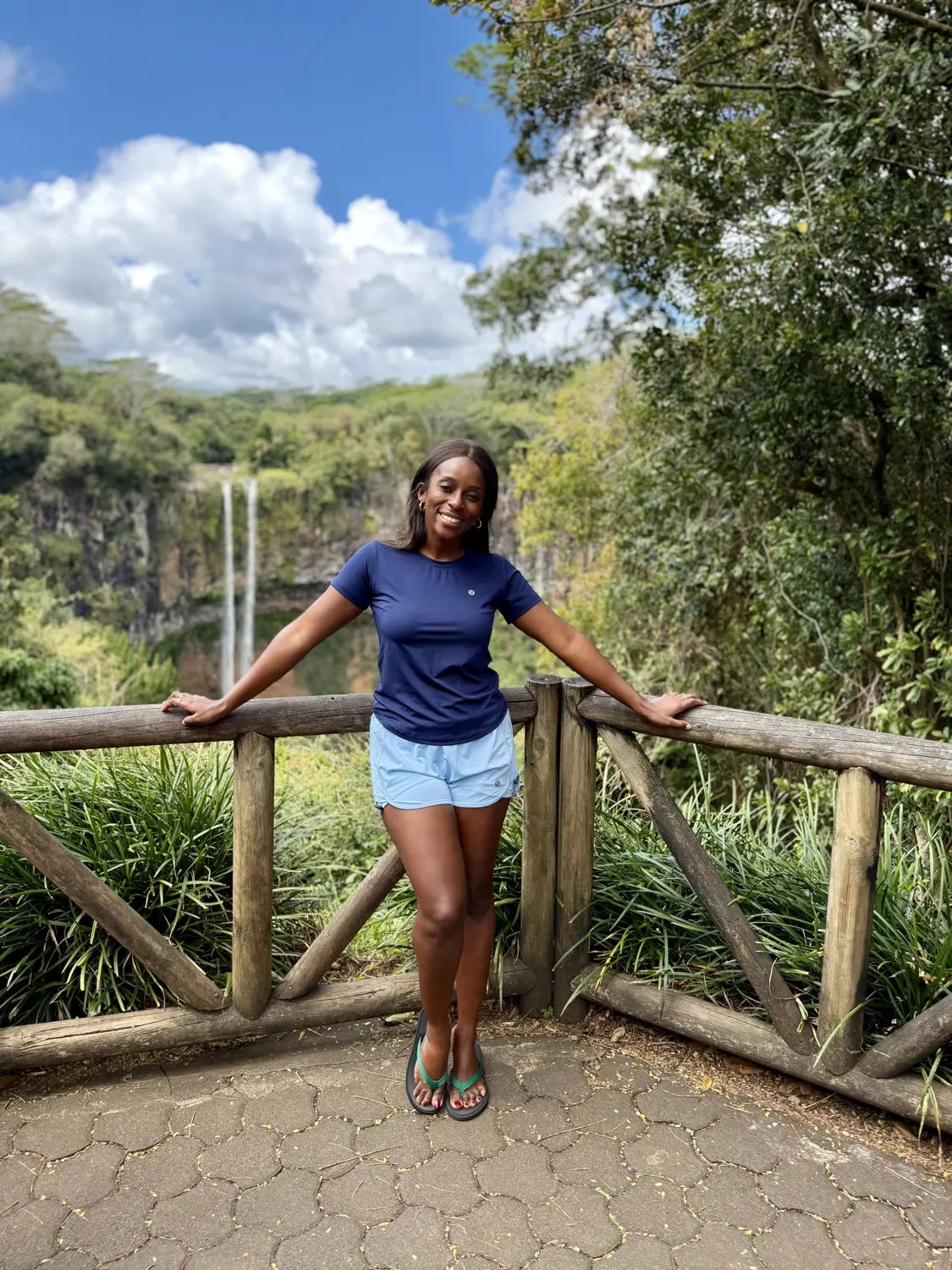 Melody leaning on a wooden railing at the Chamarel waterfall viewpoint