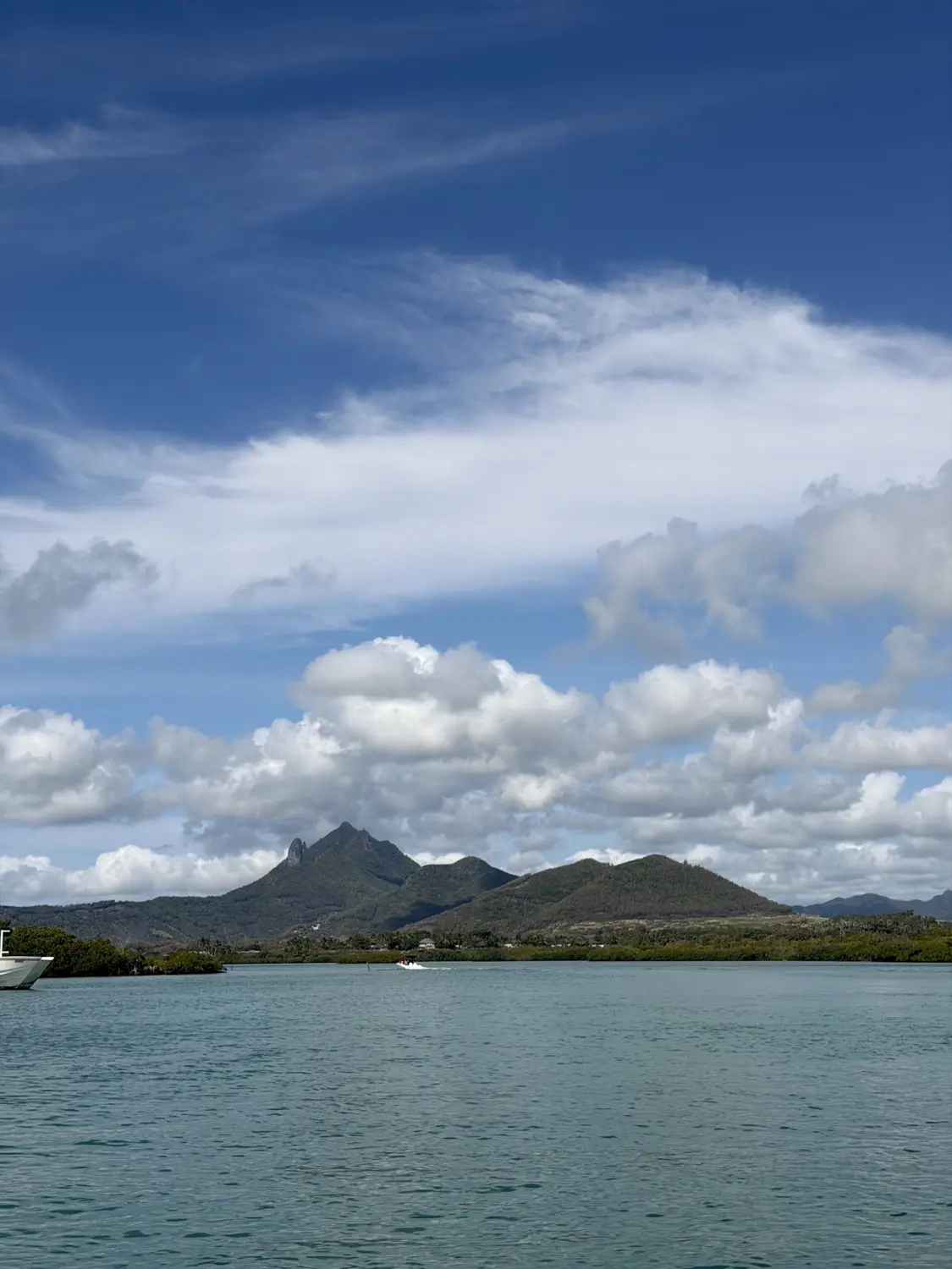 Jagged green mountains and the lagoon seen from the boat under a big blue sky
