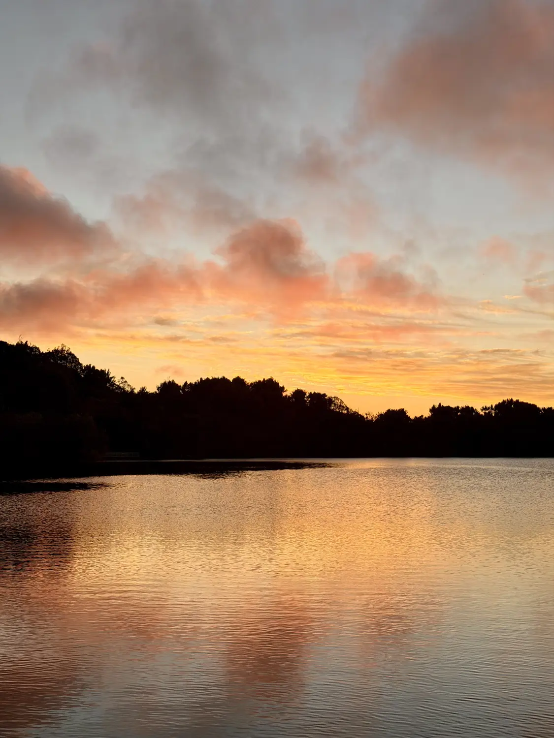 A calm highland lake reflecting a pink and orange sunset sky