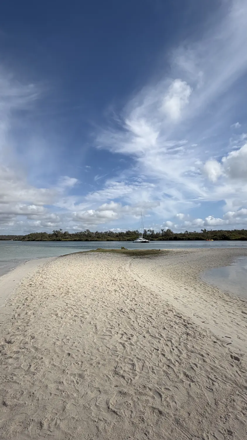 A white sandbank in the lagoon with a catamaran anchored offshore