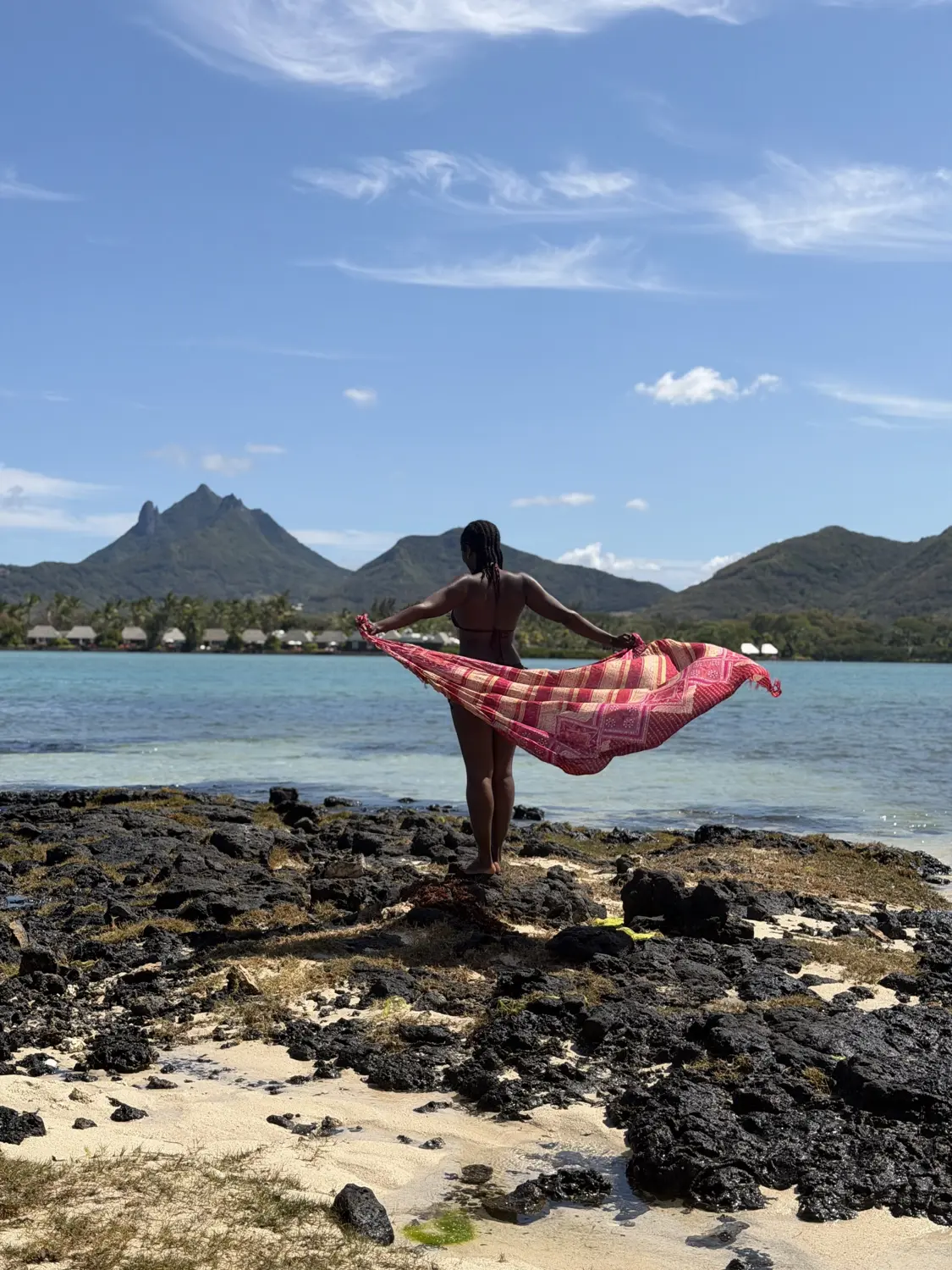 Melody on black volcanic rocks with a sarong flying in the wind and jagged peaks behind