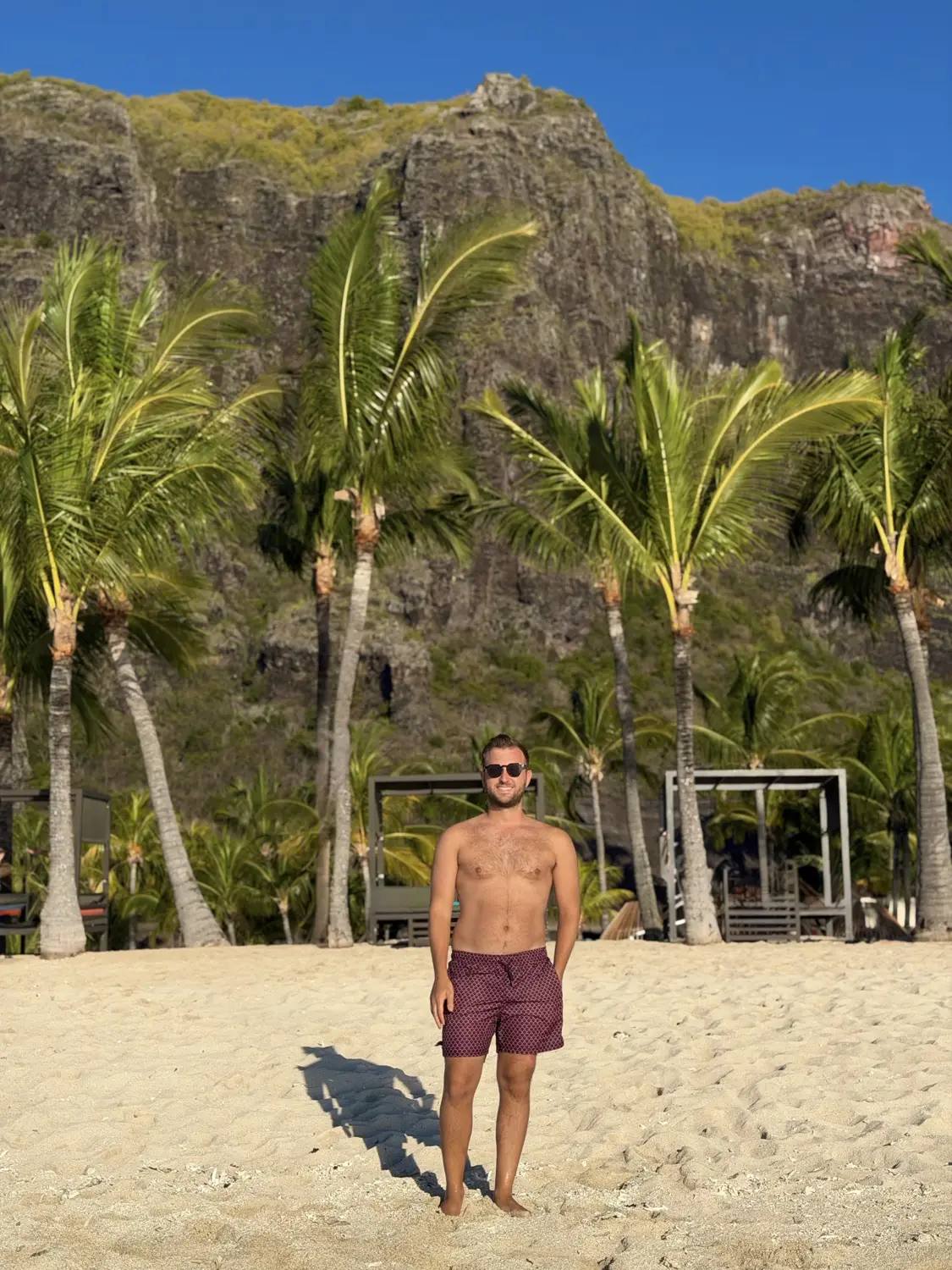 Andrew standing on the white sand in front of palm trees and the Le Morne cliffs