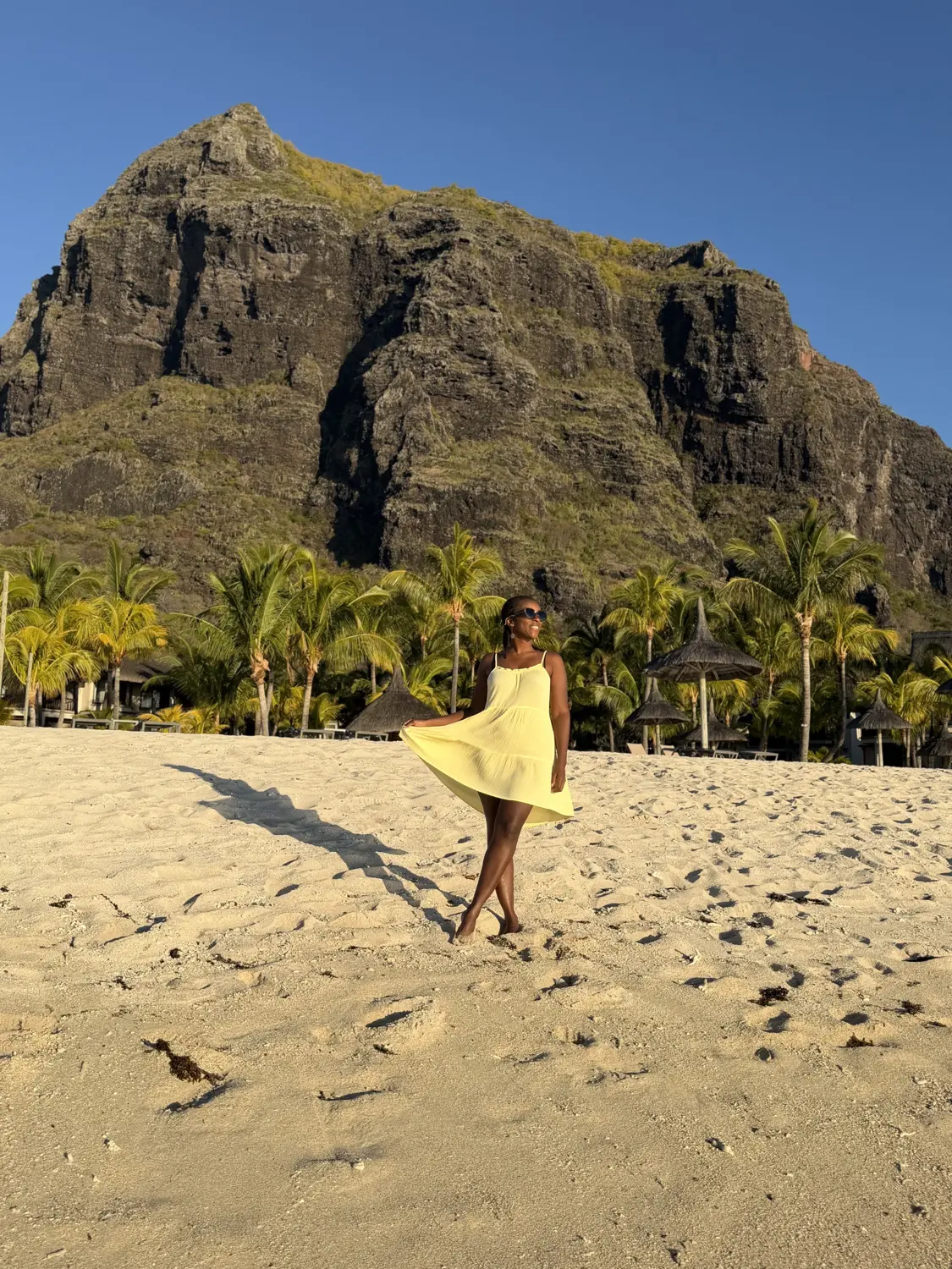 Melody twirling her yellow dress on the beach beneath the cliffs of Le Morne Brabant