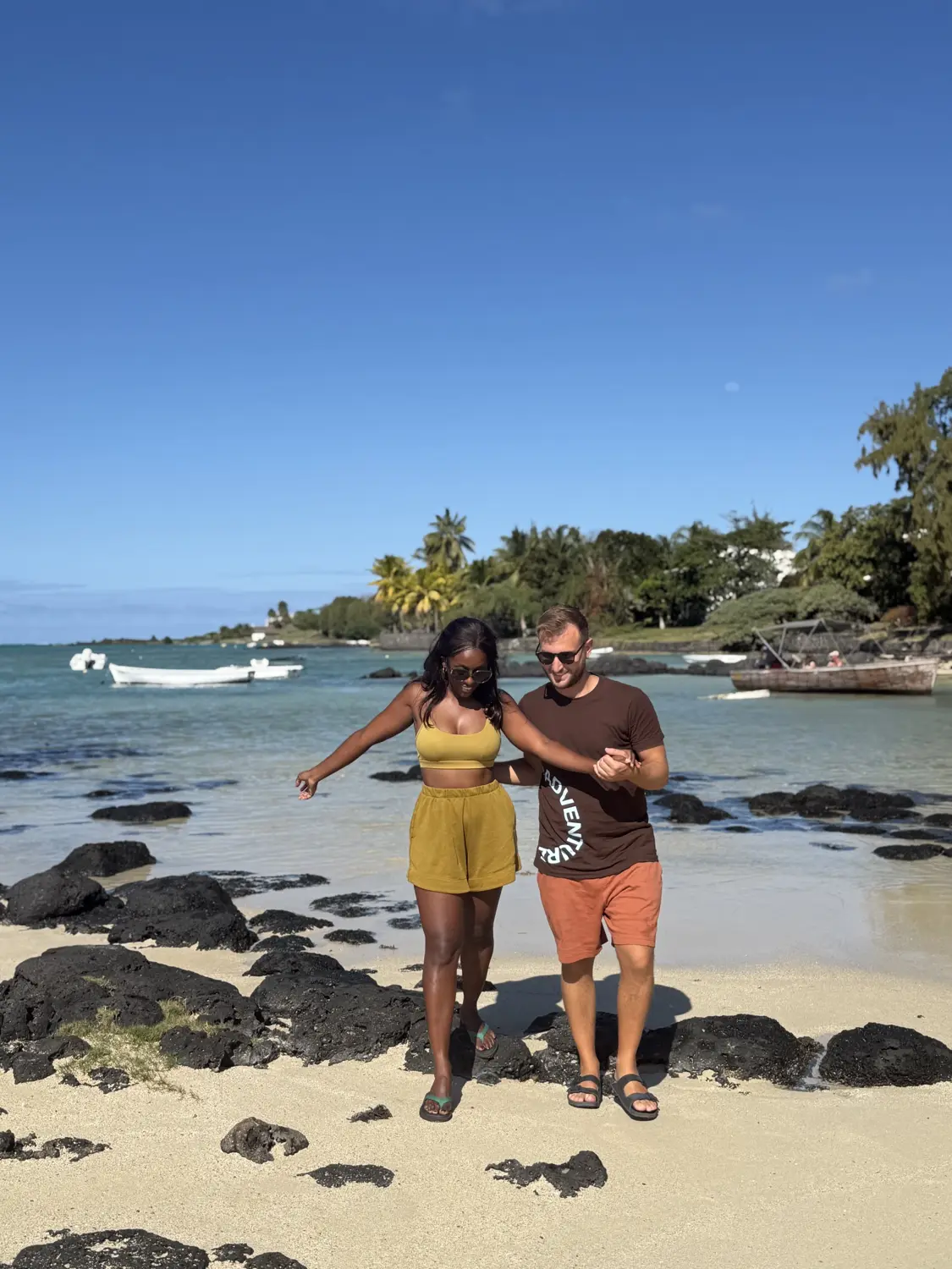 Us walking over black rocks on a north-coast beach with fishing boats in the bay
