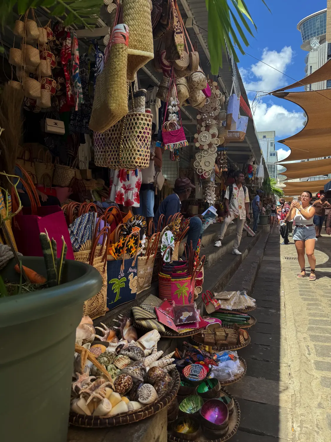 Market stalls piled with woven baskets, bags and seashells in Port Louis