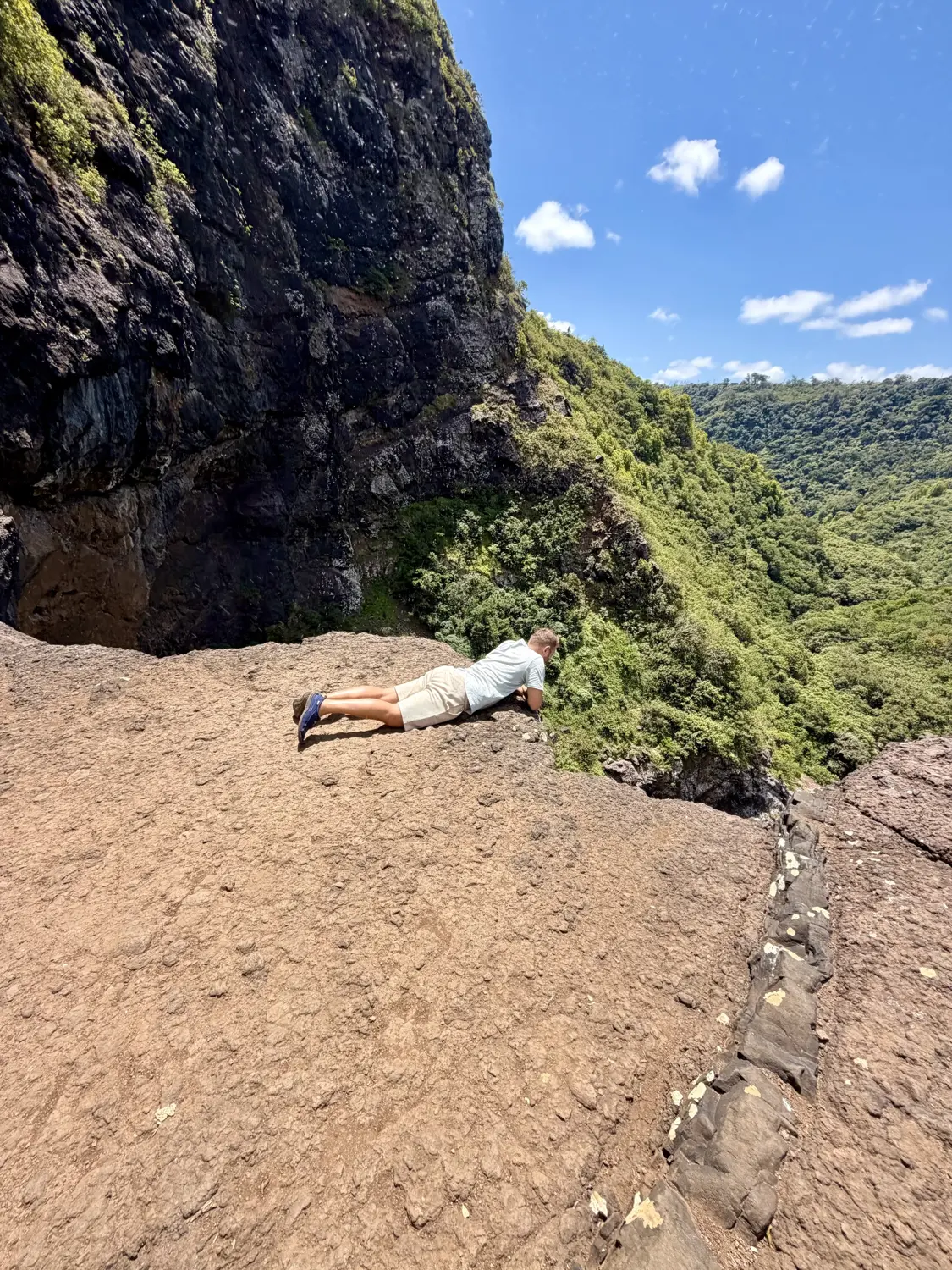 Andrew lying flat on the rock, peering over the cliff edge into the gorge