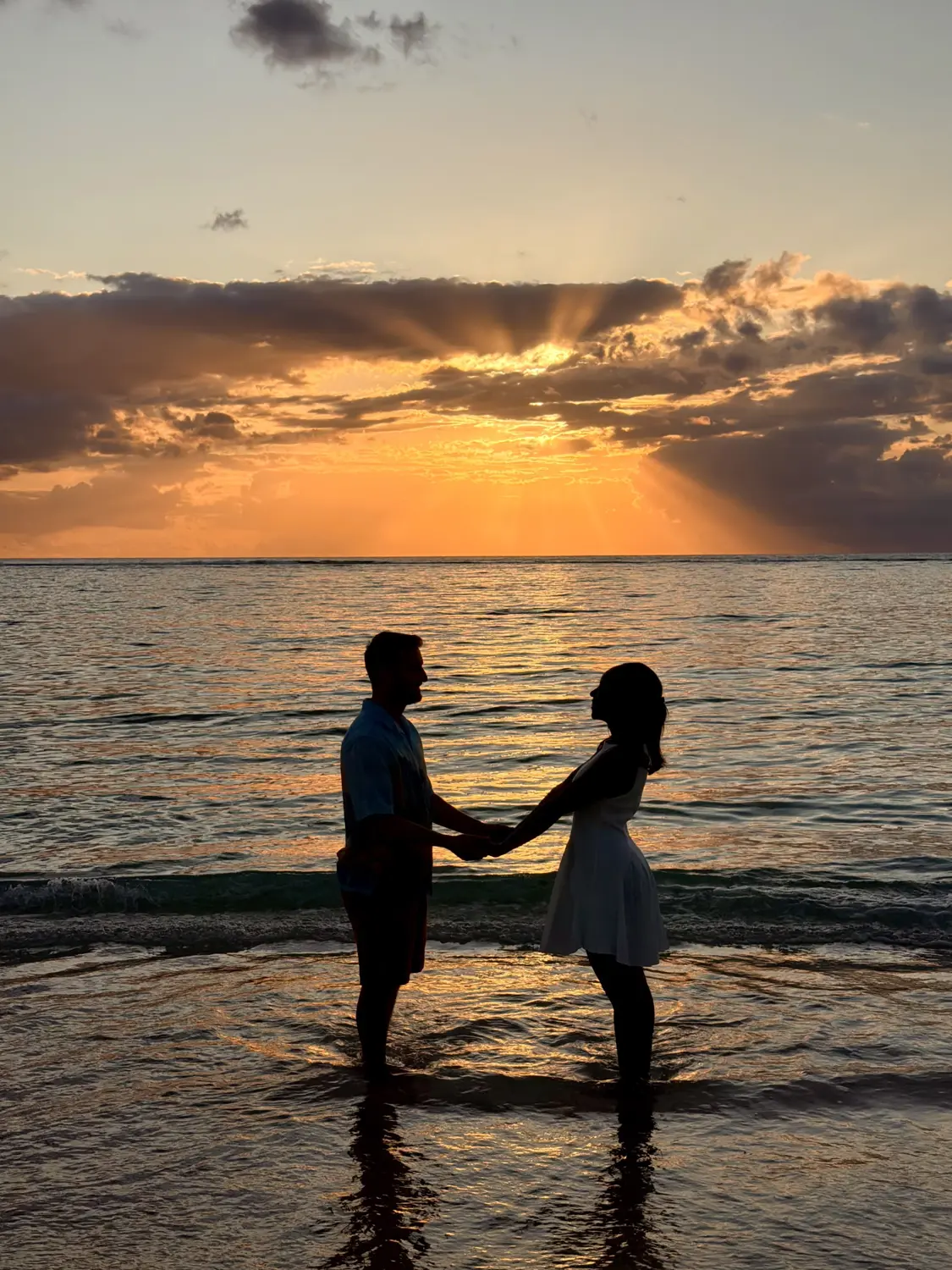 Our silhouettes holding hands in the shallow water under a glowing orange sunset
