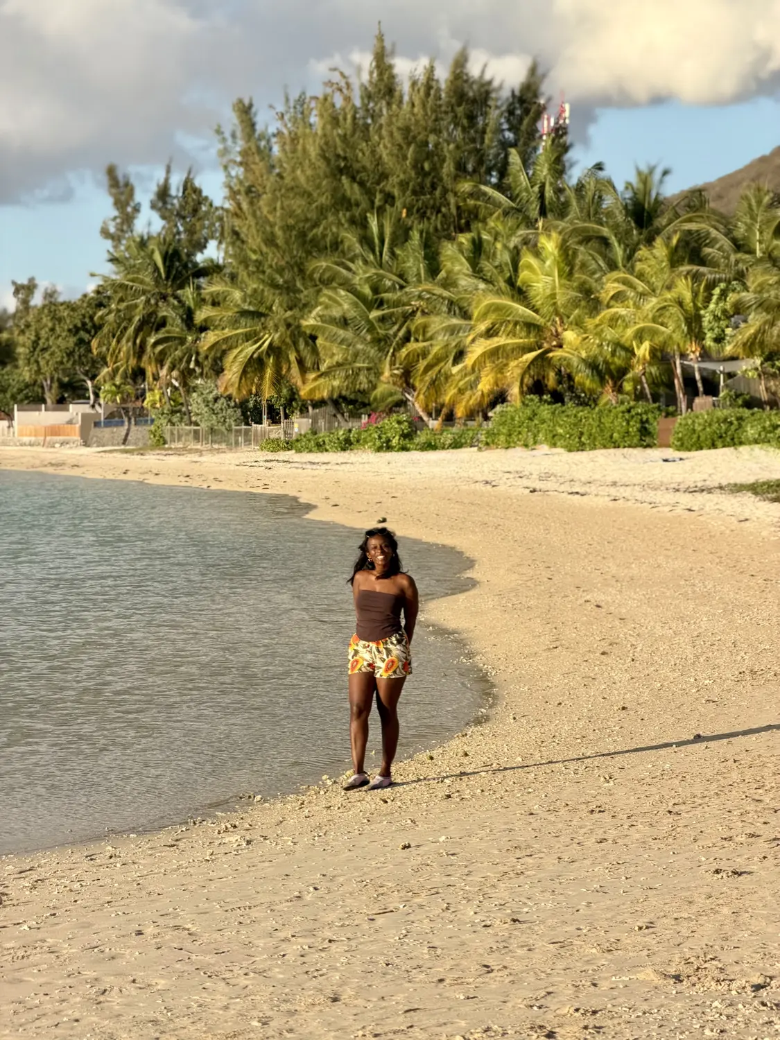 Melody walking along a curved sandy beach lined with palm trees in the late afternoon