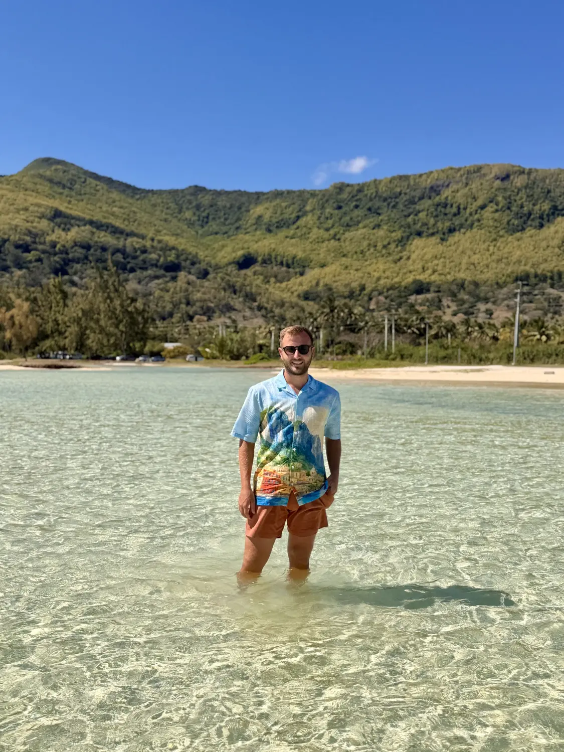 Andrew standing knee-deep in glass-clear shallow water with green hills behind