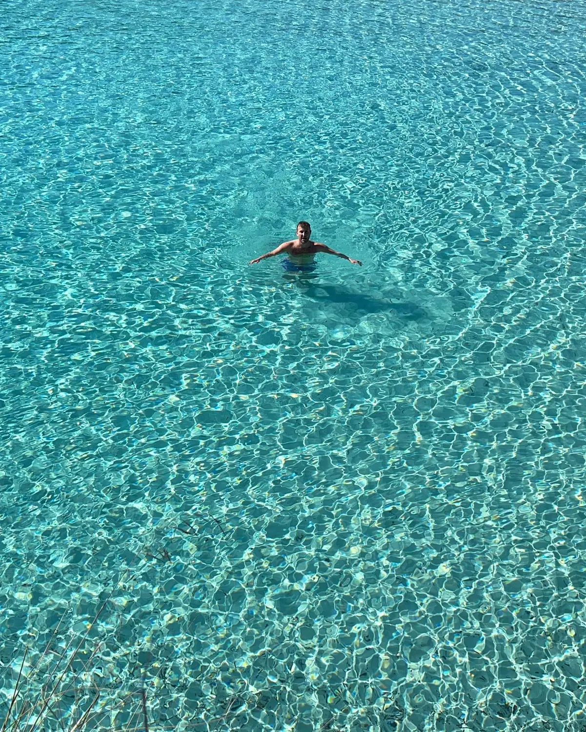 Andrew swimming in impossibly clear turquoise water seen from above in Menorca