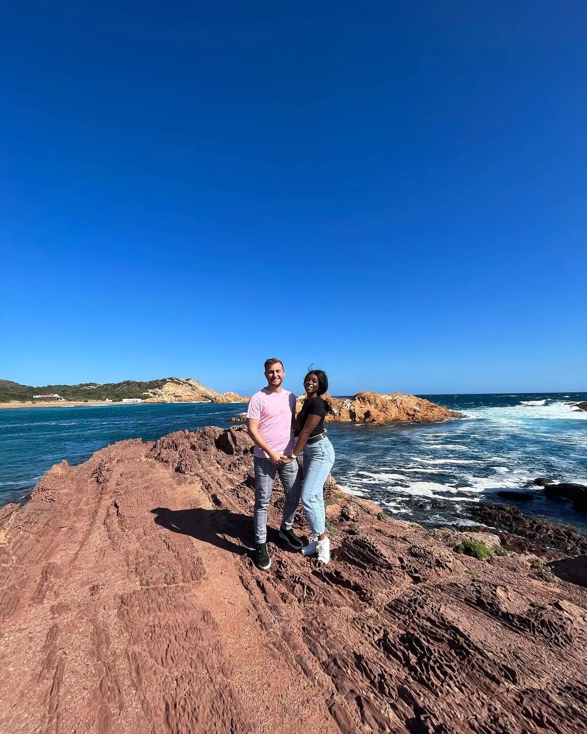 Us standing on dramatic red rock above the sea on Menorca's wild north coast