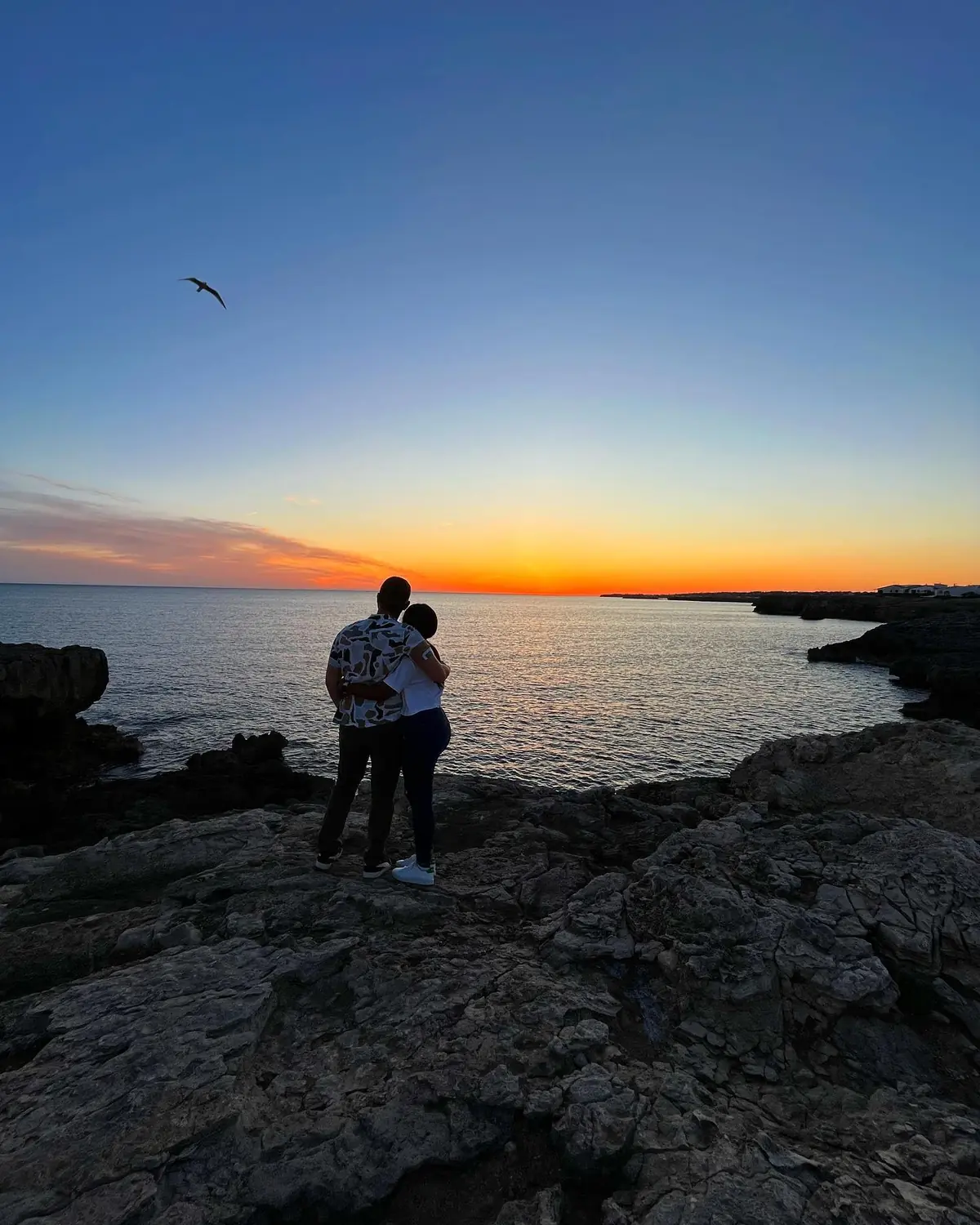 Our silhouettes watching a fiery sunset over the sea from the Menorca cliffs