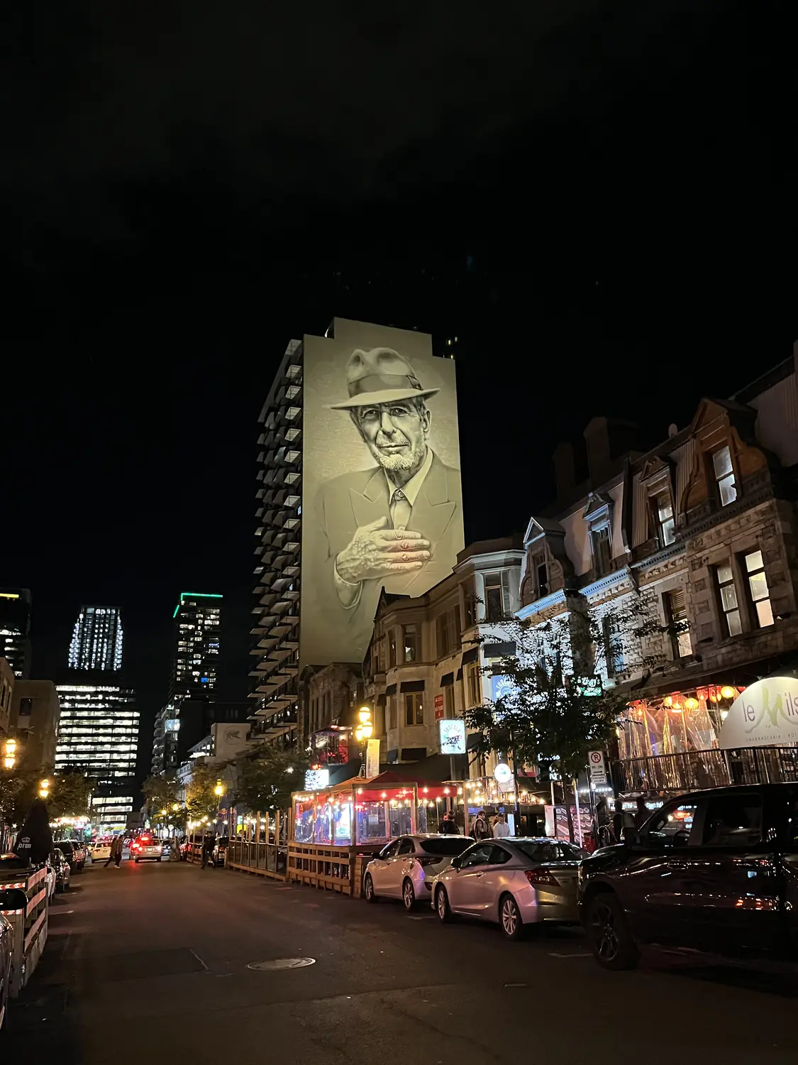 The giant Leonard Cohen mural towering over Crescent Street in downtown Montreal at night
