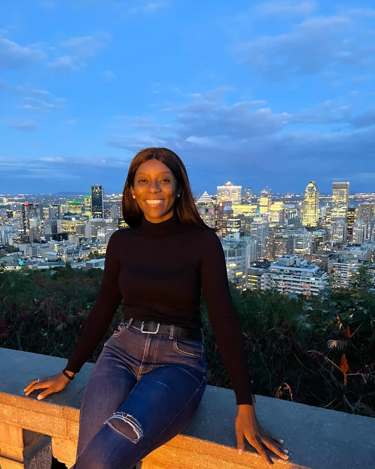 Melody on the Mount Royal lookout ledge with the Montreal skyline lit up at dusk