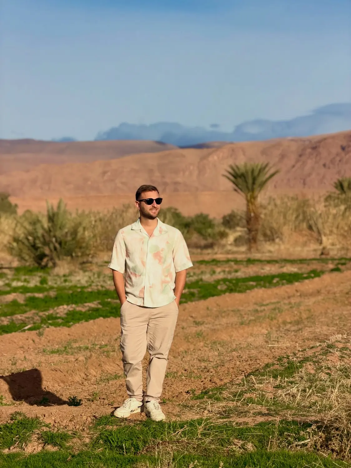 Andrew standing among palms and greenery with the desert mountains behind