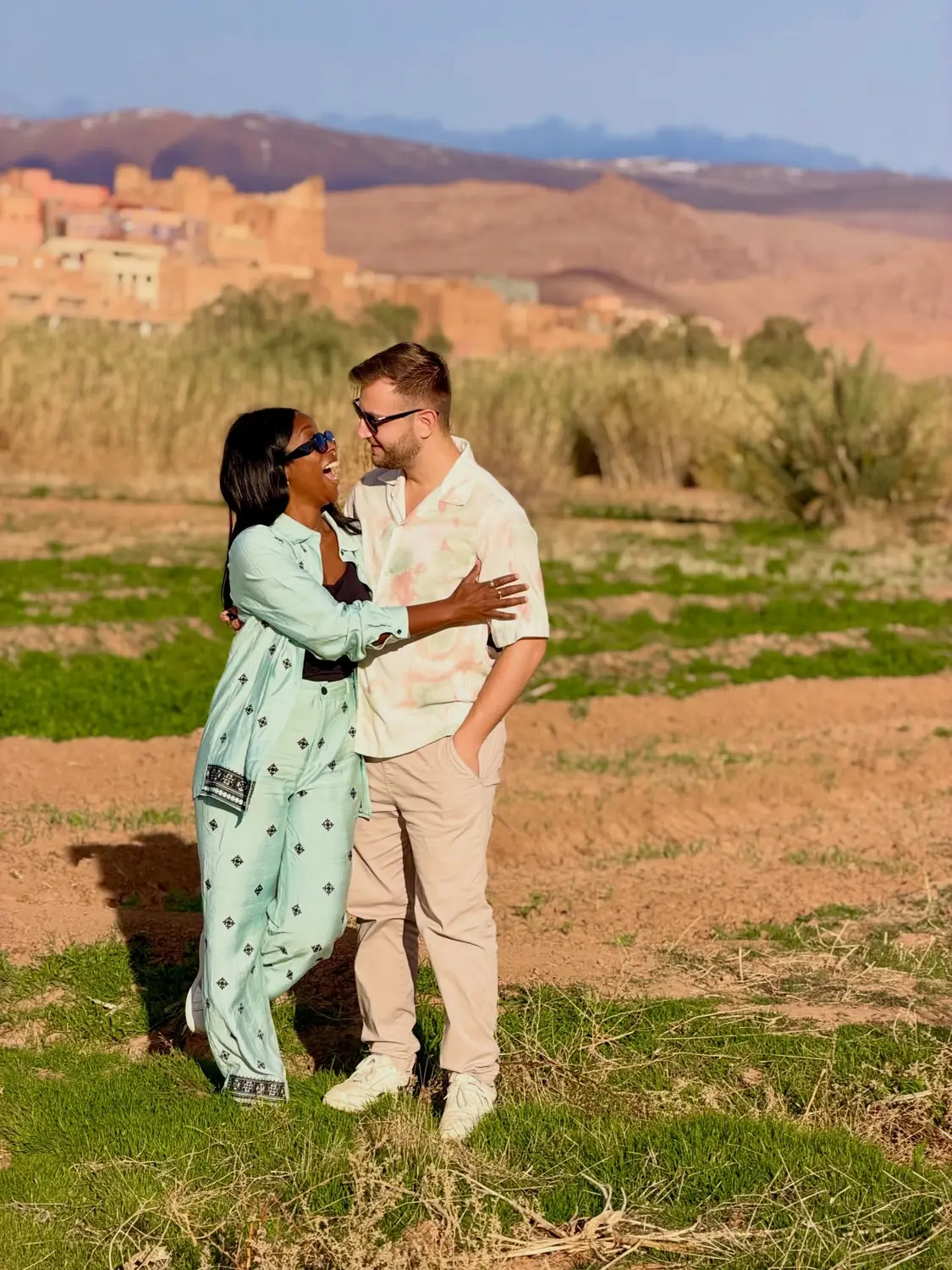 Us laughing together in a green field with a kasbah and mountains behind