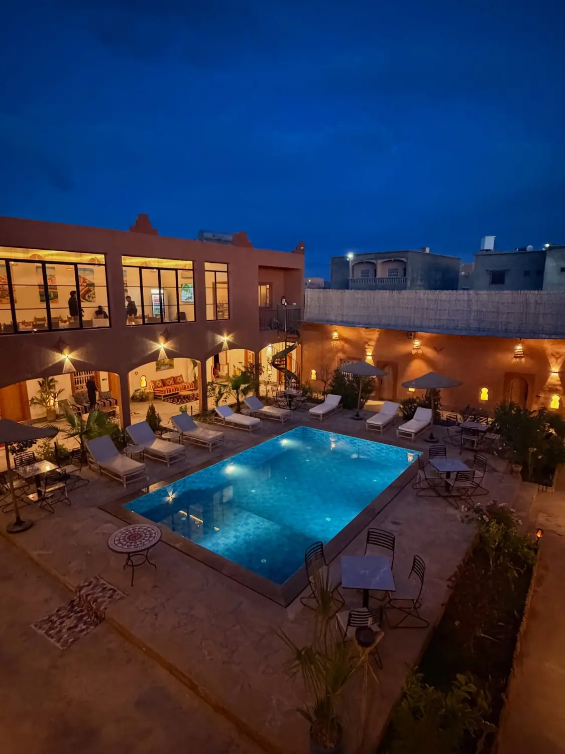 A lantern-lit kasbah hotel courtyard with a glowing blue pool at night