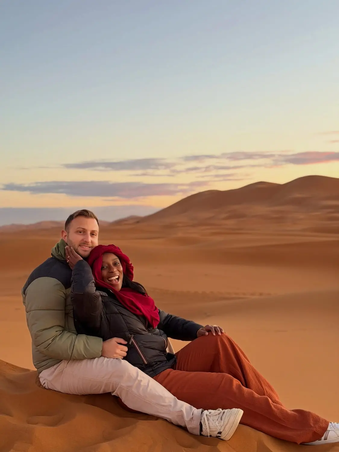 Us sitting together on a dune at sunset, Melody laughing in a red headscarf