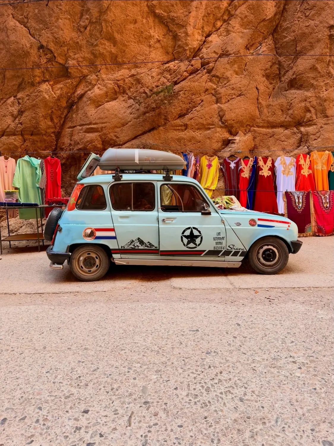 A vintage blue car parked by the Todra cliffs and hanging kaftans