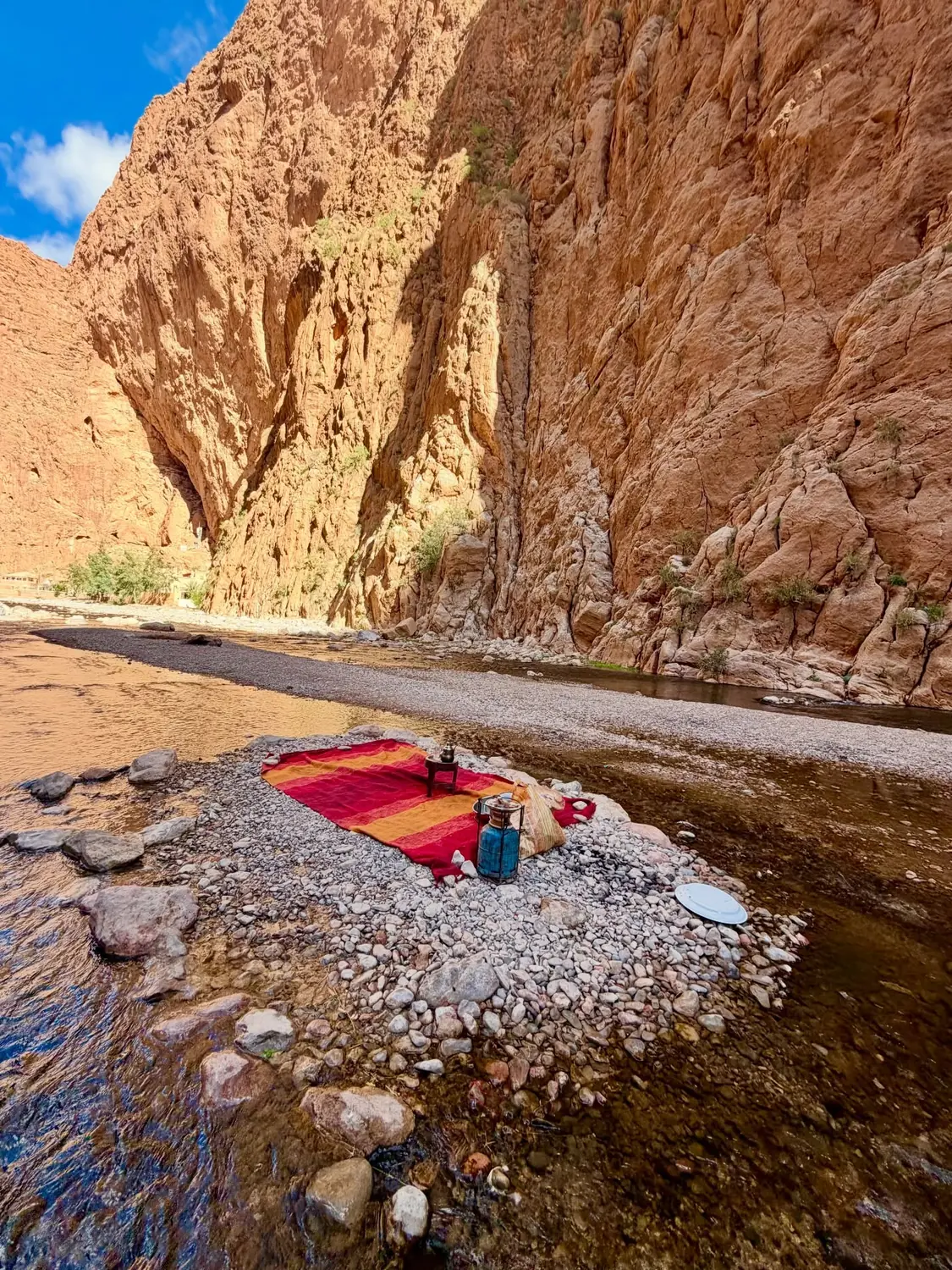 A red rug with a tea set laid out on the rocks beside the river in the Todra Gorge