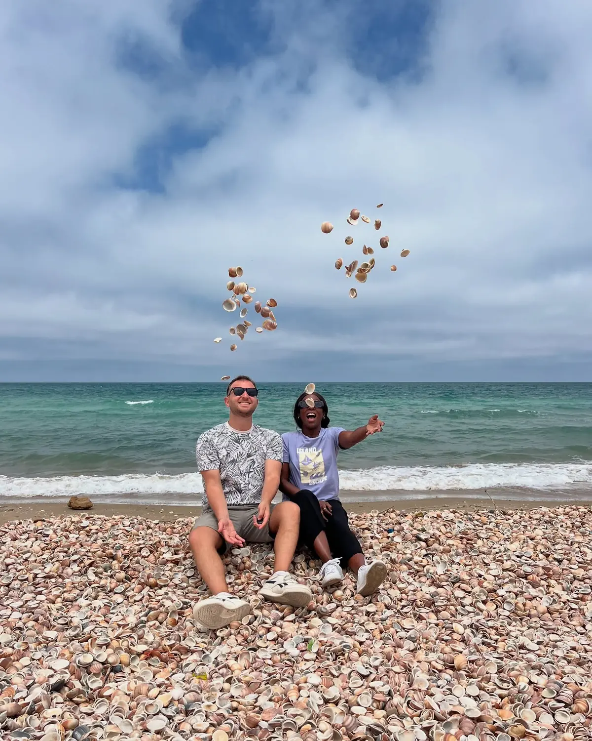 Us sitting on a beach made entirely of seashells, tossing handfuls into the air