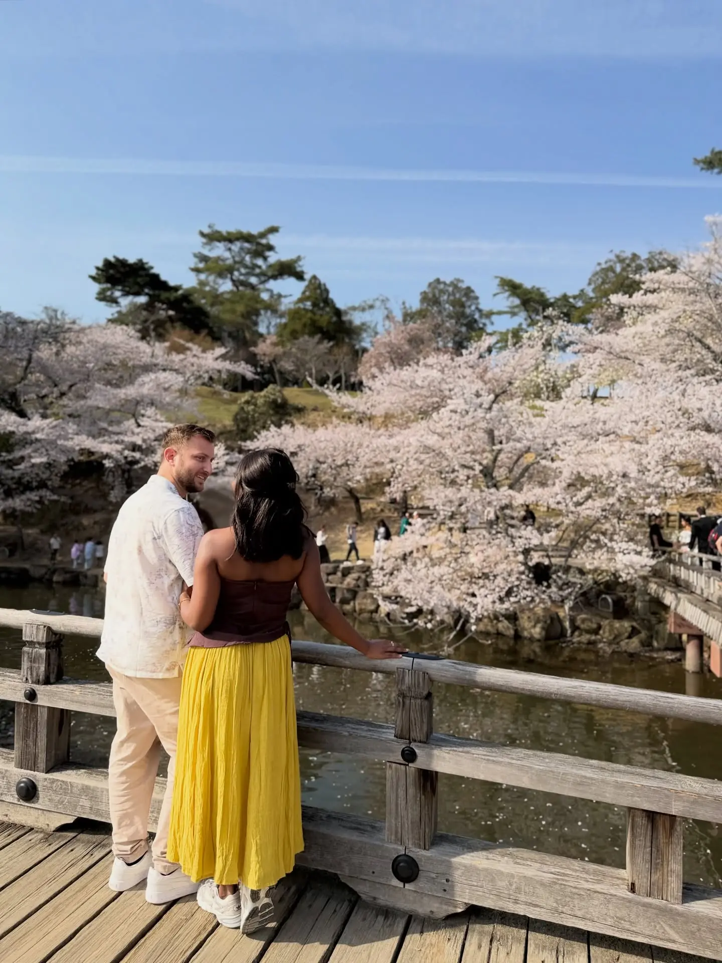 Us on a wooden bridge over a pond framed by cherry blossoms in Nara