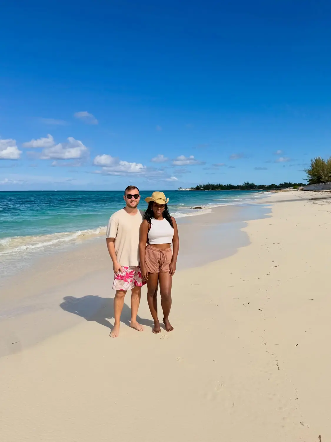 Us standing barefoot on an empty powder-white beach with calm blue water