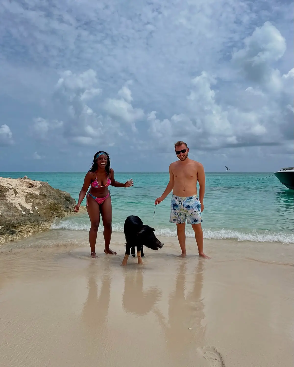 Standing with a black swimming pig on the beach, boat moored behind