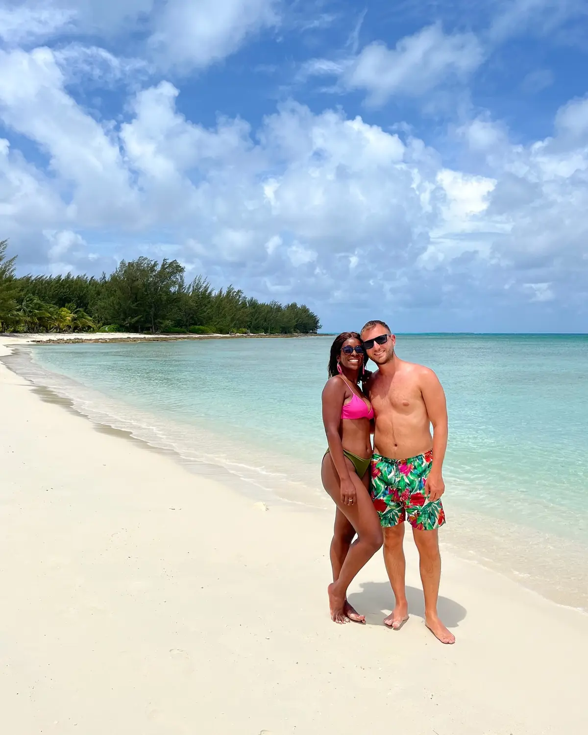 Us on a wide stretch of white-sand beach backed by a green treeline