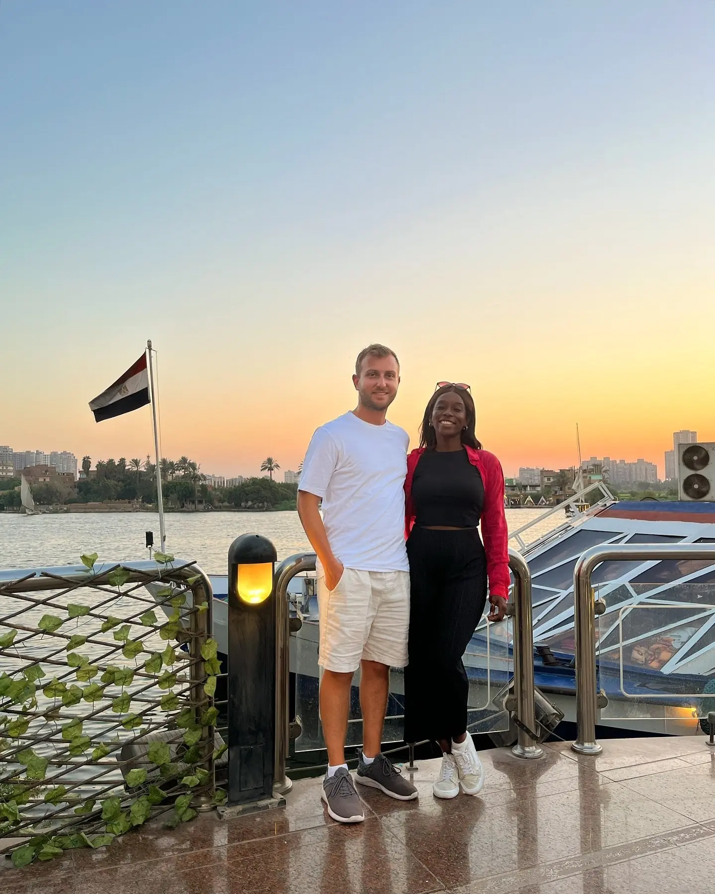 Couple by the Nile at sunset with an Egyptian flag and a boat