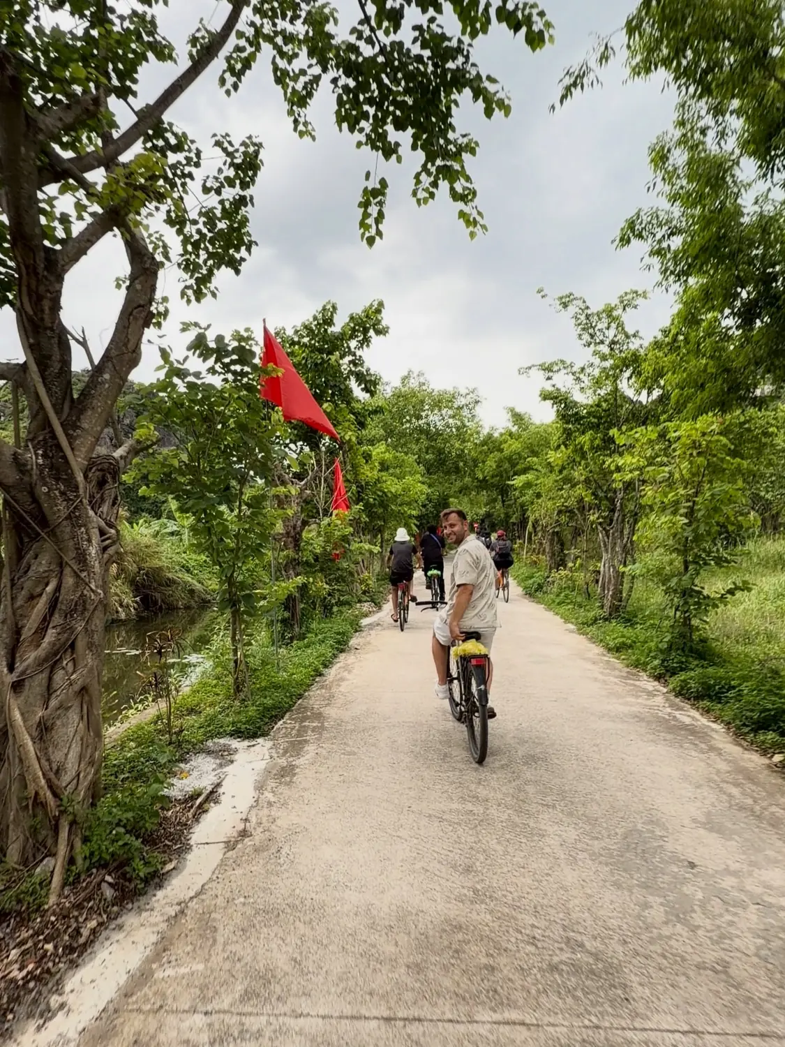 Andrew cycling a quiet lane past red flags and rice paddies in the Ninh Binh countryside