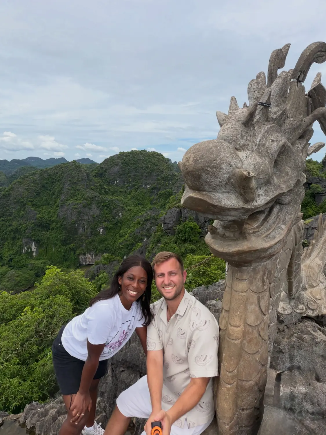 Us at the Mua Cave viewpoint beside the carved stone dragon, karst peaks behind