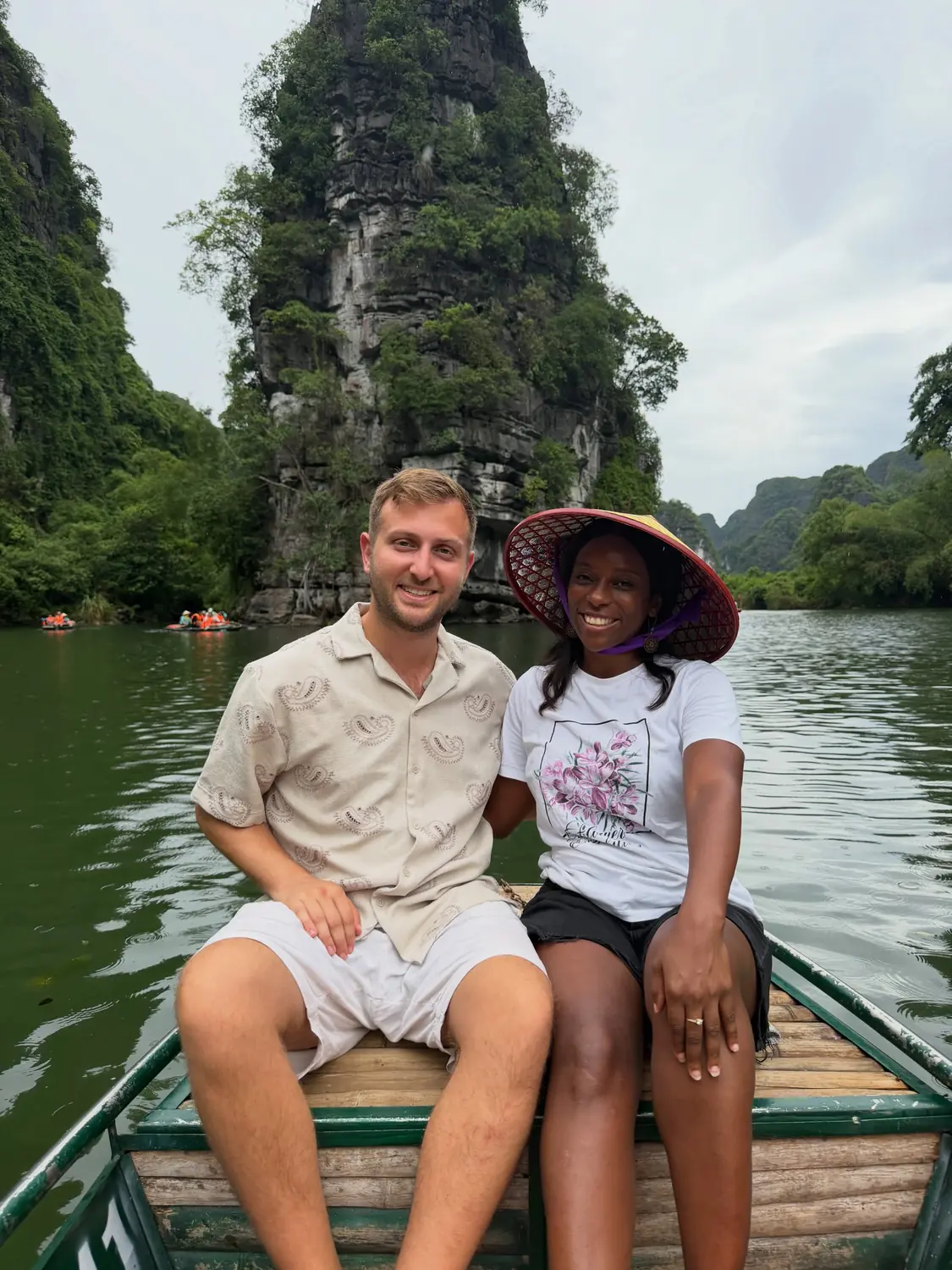 Us on a rowboat gliding past a towering limestone karst in Trang An