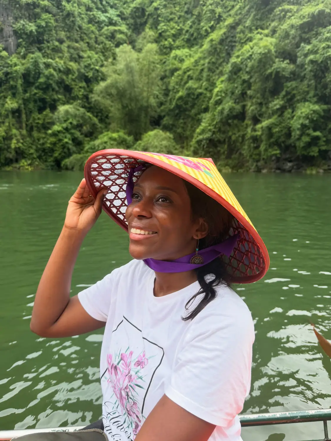 Melody in a colourful conical hat on the boat, green river behind